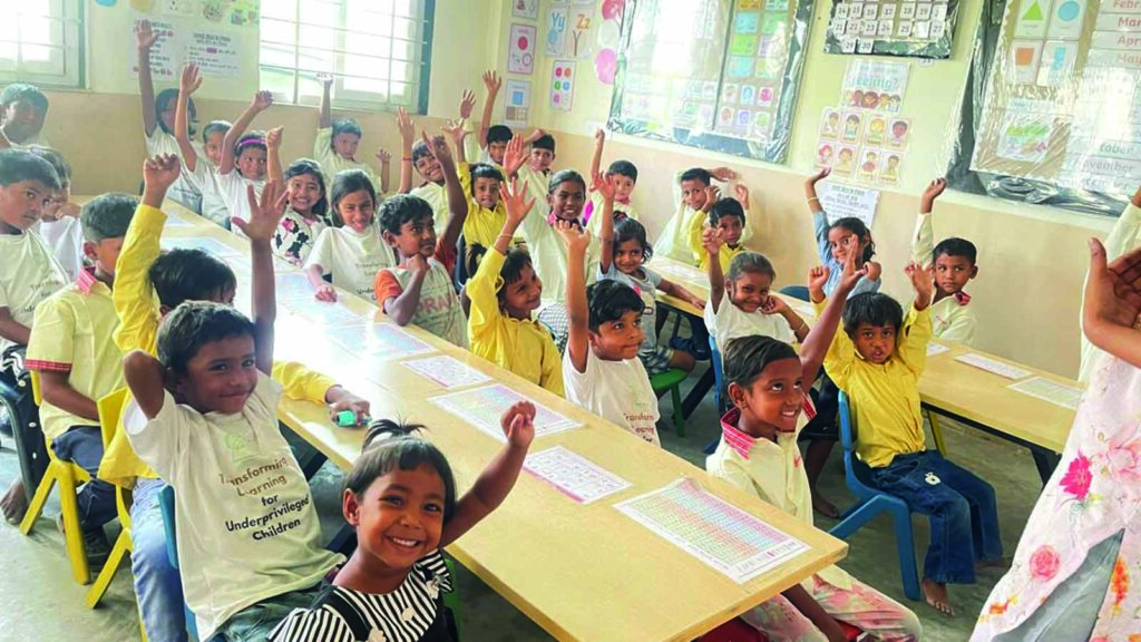 A classroom of smiling underprivileged children at SMB Foundation Rohini centre raising their hands during a joyful learning session in Delhi.