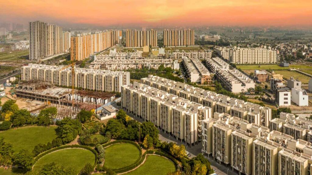 Aerial view of Wave City Ghaziabad showing residential towers, villas, and green parks during sunset.